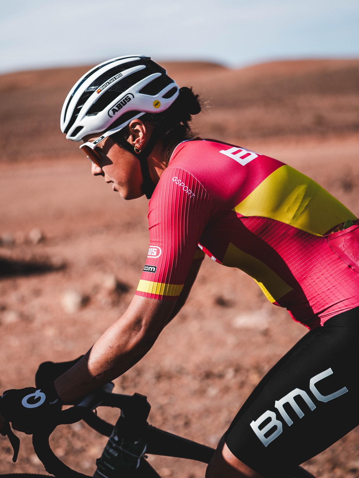 Marta Torà Milà racing in the red and yellow Spanish national kit on a dusty gravel road